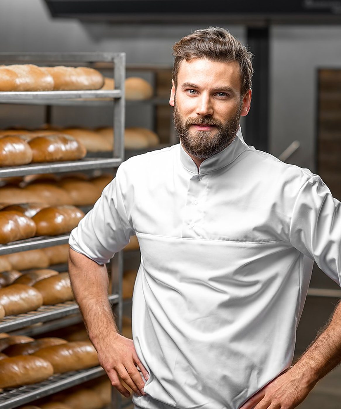 Boulanger barbu en veste blanche devant des étagères de pains